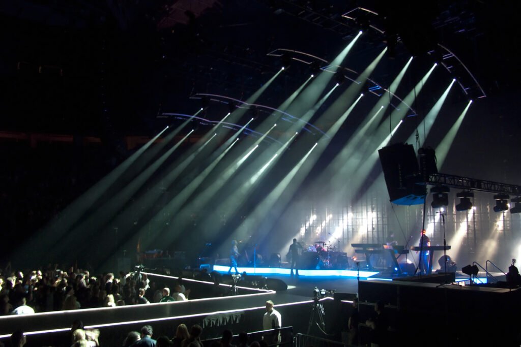 A vibrant stage illuminated by spotlights during a live concert. Musicians perform in front of a large audience.