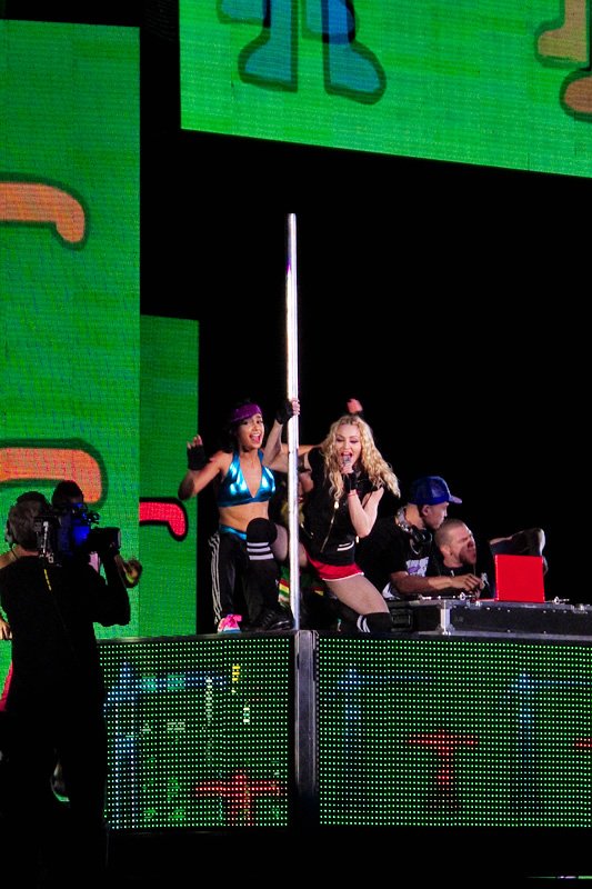 Performers on stage during a vibrant live music event with colorful lighting and energetic crowd.