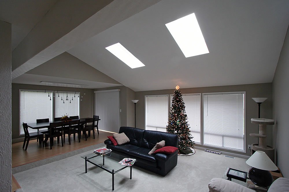 A modern living room featuring skylights, a black leather sofa, and a dining area in the background.