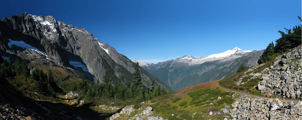 A stunning view of rugged mountains and a clear blue sky from a rocky trail.