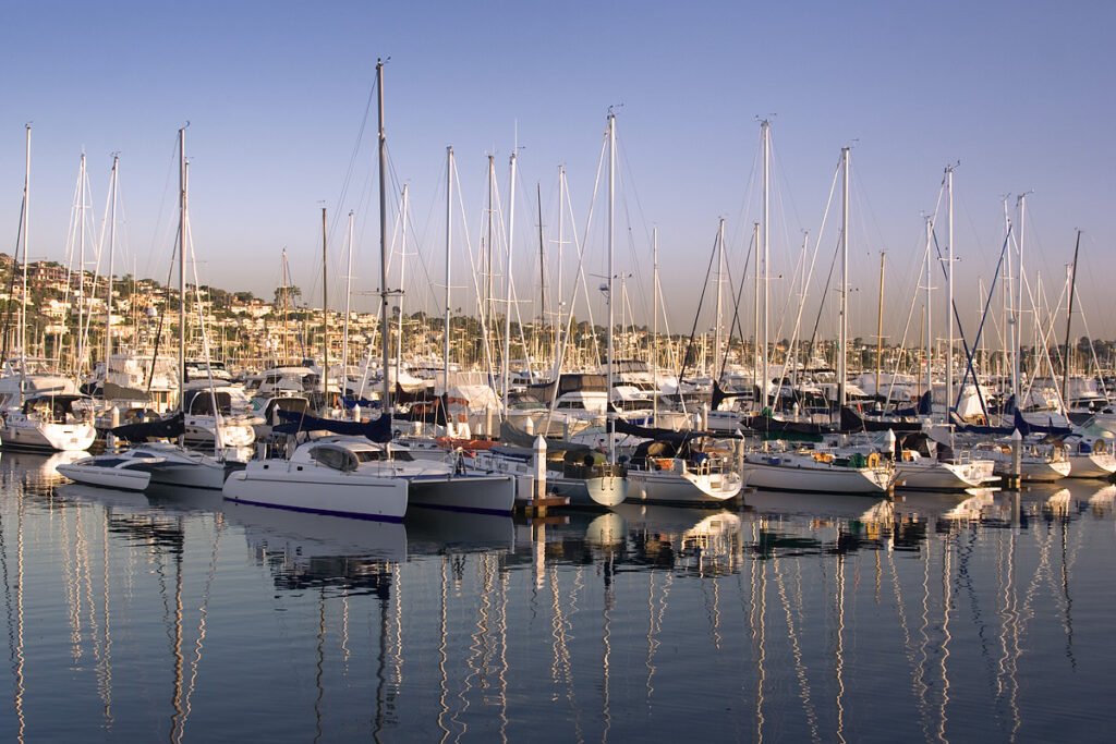 A tranquil marina filled with sailboats reflecting in the calm water under a clear sky.