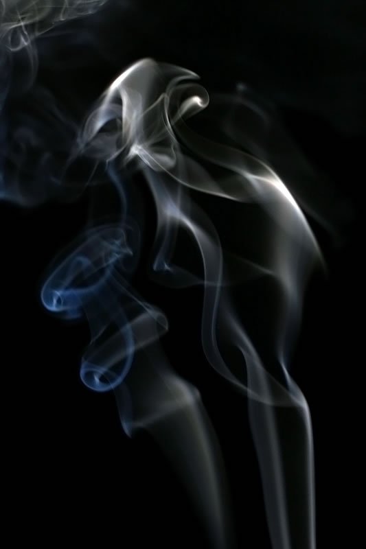 Smoke swirling and twisting in intricate patterns against a dark backdrop, creating a dynamic visual effect.