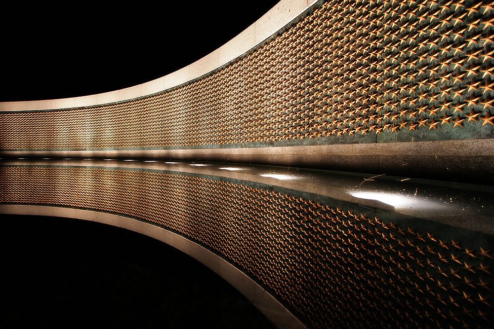 A close-up view of a metallic surface with a reflective, textured pattern. The image captures the intricate details of the material's design and its glossy finish.