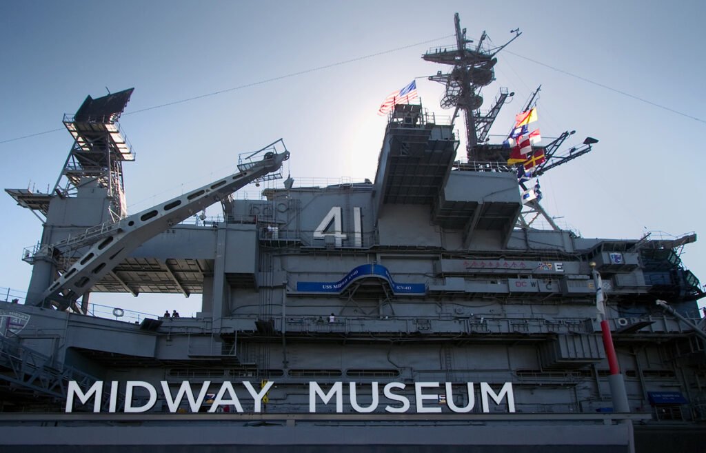 The Midway Museum, featuring a historic aircraft carrier with its distinctive superstructure and flags flying high.