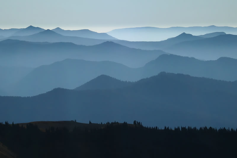A serene view of layered mountains shrouded in mist, captured at dusk.