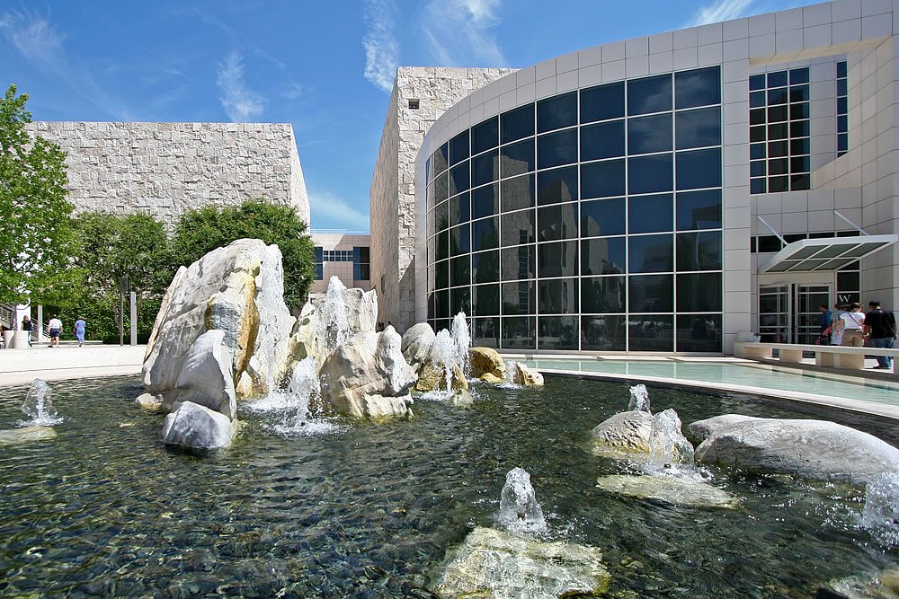 A modern architectural building features large glass windows and is complemented by a serene reflecting pool and decorative fountain.