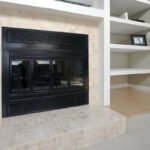 A cozy living space featuring a sleek black fireplace flanked by elegant white built-in shelves. The scene is complemented by warm wood flooring and soft carpeting.