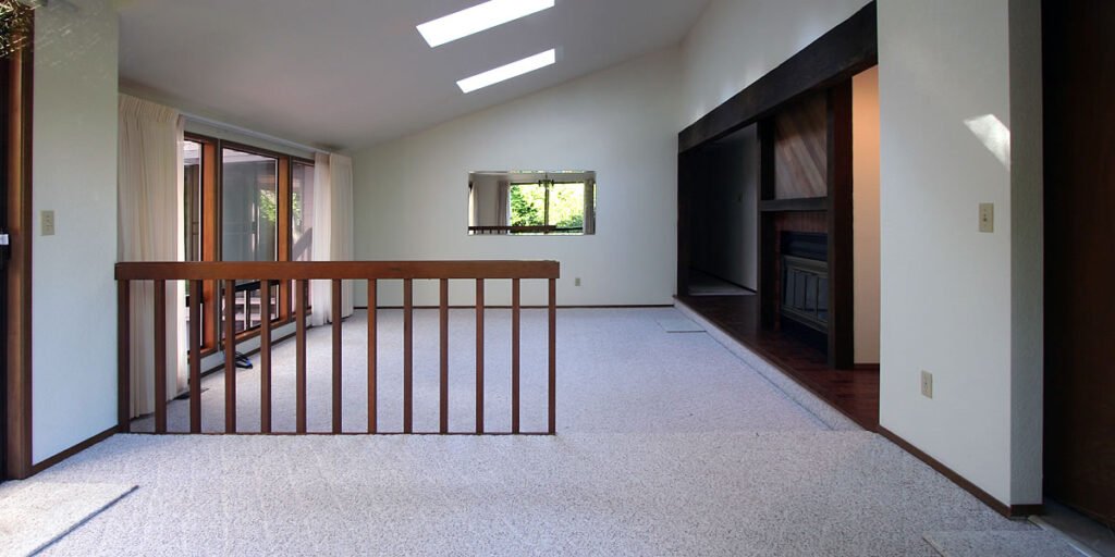 A spacious loft area with carpeted flooring, framed by wooden railings and skylights that let in natural light.