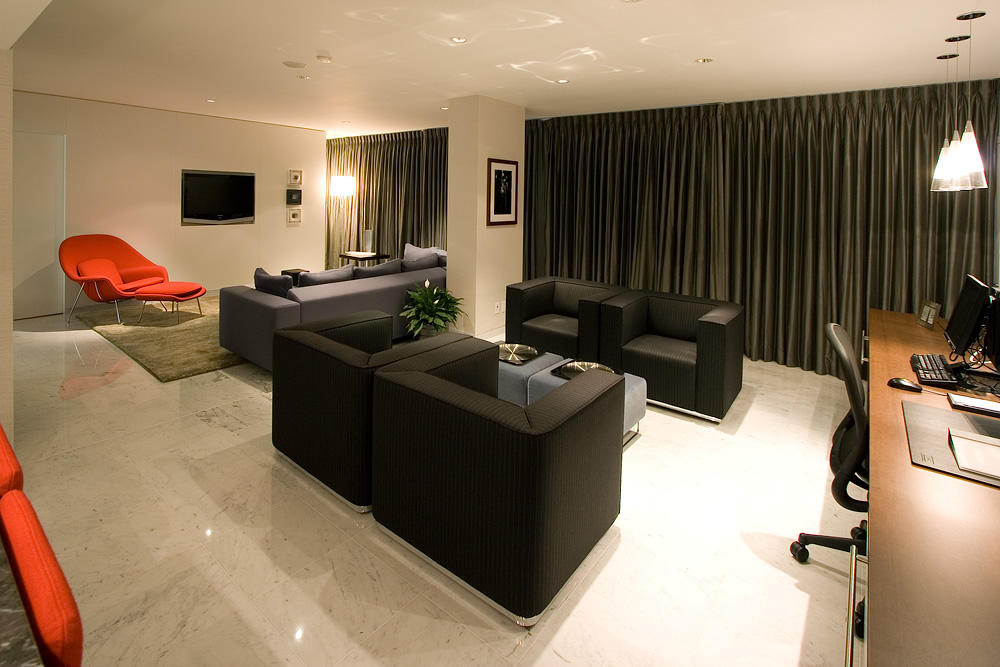 A spacious and modern living room with sleek black furniture, a bright red armchair, and elegant interior lighting.