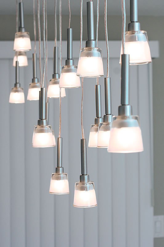 A group of modern pendant lights with frosted glass shades hanging from a ceiling, casting a warm glow over a light-colored interior.