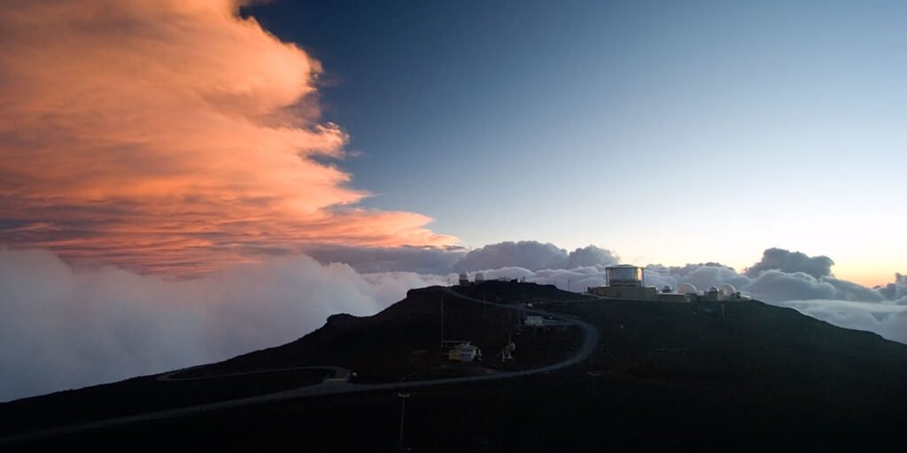 A stunning sunset view of Mount Rainier, silhouetted against a vibrant sky with fluffy clouds. The mountain's peak is partially covered by mist, creating a magical atmosphere.