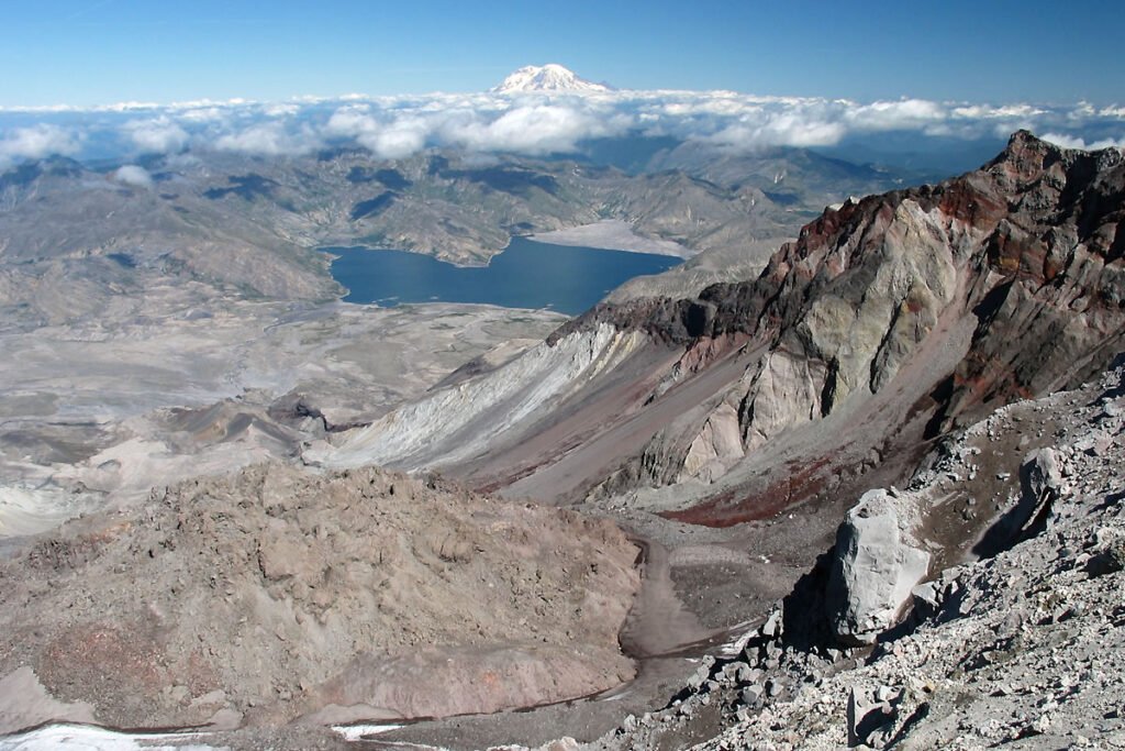 A breathtaking panoramic view of Mount St. Helens crater with a serene lake below and distant snow-capped peaks.