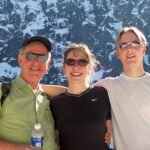 White Salmon Ridge Three smiling individuals posing in front of a stunning snow-covered mountain landscape.