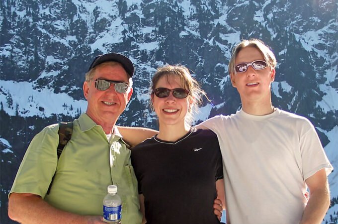 Three smiling individuals posing in front of a stunning snow-covered mountain landscape.