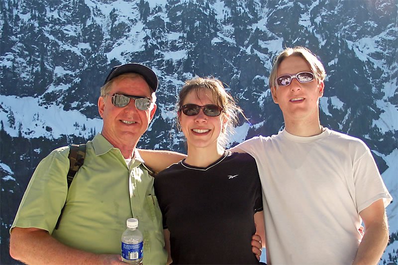 Three smiling individuals posing in front of a stunning snow-covered mountain landscape.