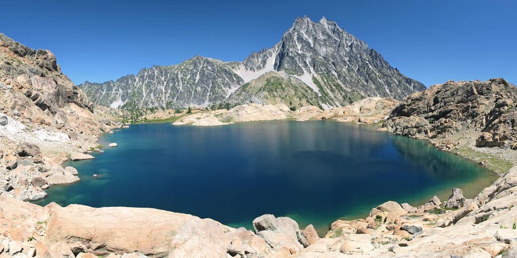 A stunning view of a crystal-clear mountain lake surrounded by rugged peaks under a clear blue sky.