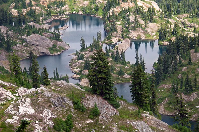 A scenic view of tranquil mountain lakes surrounded by rocky terrain and evergreen trees, reflecting the calm waters.