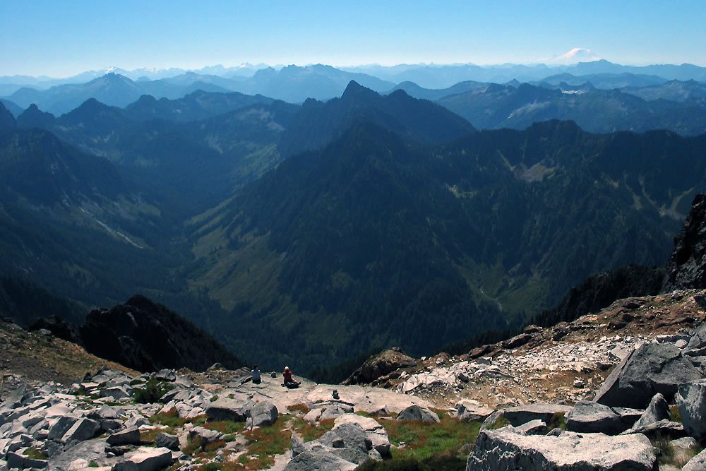A stunning panorama of rugged mountain peaks under a clear blue sky, showcasing the vastness and beauty of nature from an elevated rocky summit.