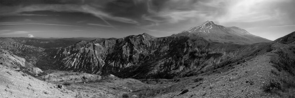 A stunning black-and-white photo showcasing rugged mountain peaks and valleys under a cloudy sky.