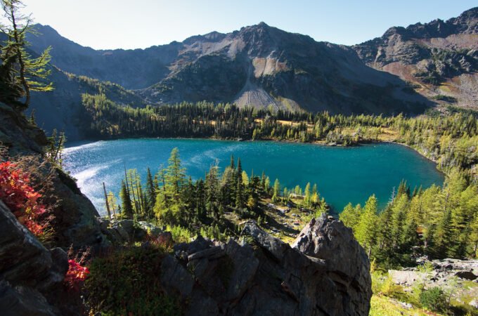 A stunning view of a turquoise mountain lake surrounded by lush forests and towering peaks.
