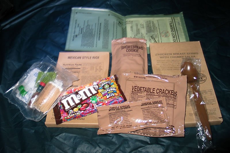 A prepared MRE meal featuring crackers, M&Ms, and vegetables laid out on a blanket.