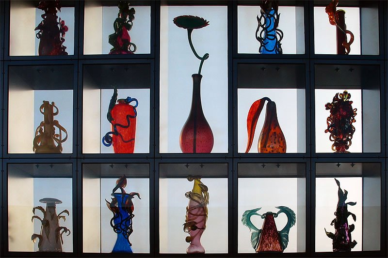 A vibrant array of hand-blown Murano glass sculptures artfully arranged in a grid-like showcase with varying shapes and colors.