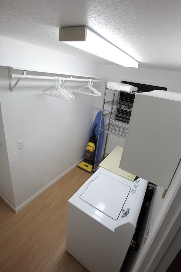 A converted walk-in closet with open shelving and a top-loading washing machine.