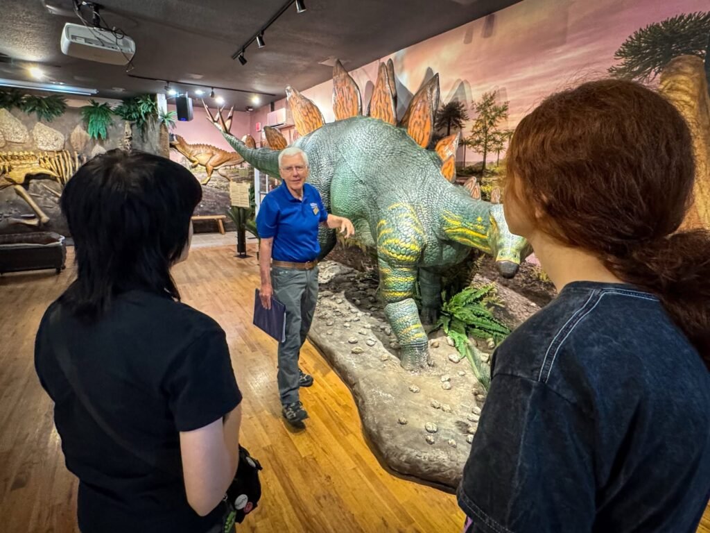 A couple explores dinosaur exhibits with a guide at a museum.