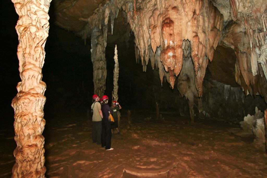 A group of people wearing red hats explore a cave with impressive stalactites and stalagmites. The formations highlight the natural beauty of the cavern.