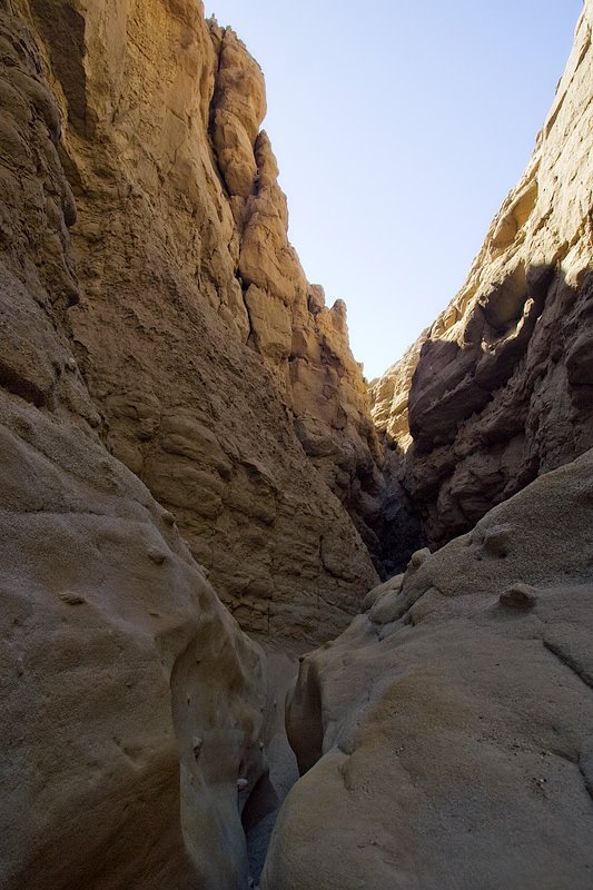 View of a narrow canyon with towering rock walls and a clear blue sky above.