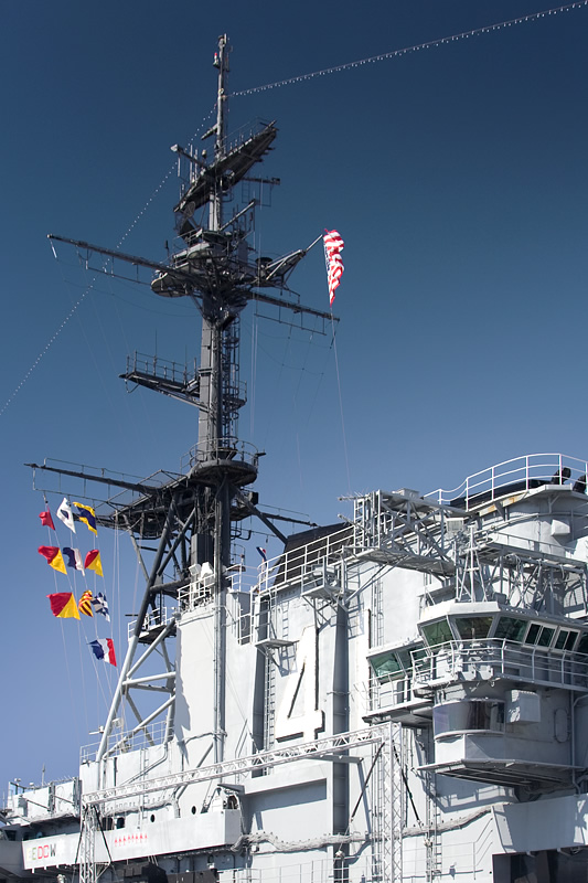 A close-up view of a navy ship's radar array and flagpole against a clear blue sky.