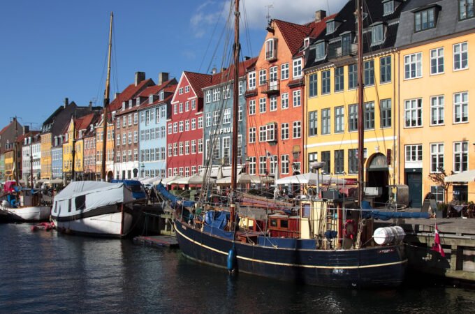 Vibrant boats docked along a canal with colorful buildings in the background under a clear blue sky.