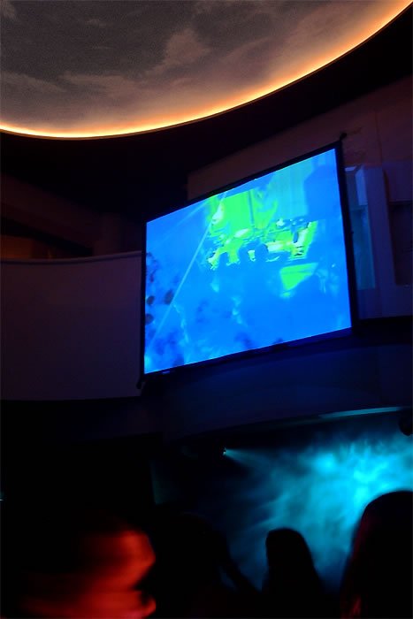 A large dome screen displays an oceanic theme with blue hues, simulating an underwater experience in a dark room.