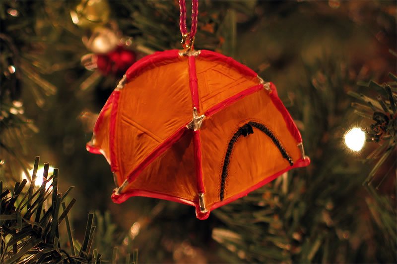 A vibrant orange tent-shaped ornament hangs from a decorated Christmas tree. It adds a playful touch to the festive decorations.