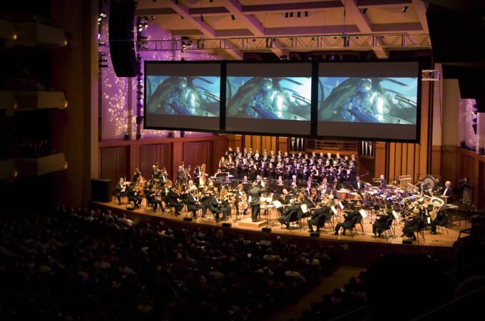 A live performance featuring an orchestra and choir on stage before a large audience.