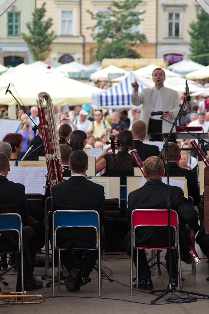 A group of musicians playing instruments with a conductor leading them in an outdoor setting.
