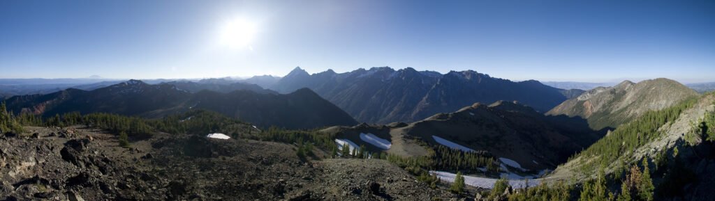 A breathtaking panoramic view of rugged mountains and serene lakes in the Pacific Northwest under a clear blue sky.