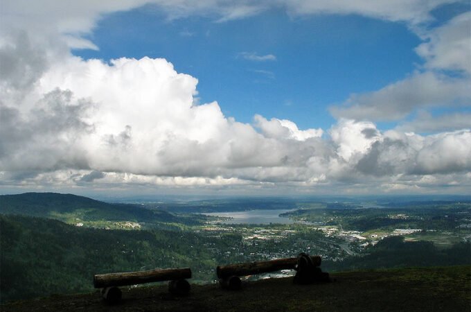 A panoramic view from a hilltop overlooking the Pacific Northwest landscape with benches in the foreground.