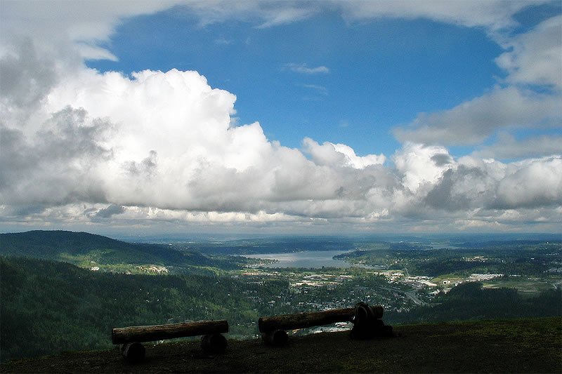 A panoramic view from a hilltop overlooking the Pacific Northwest landscape with benches in the foreground.