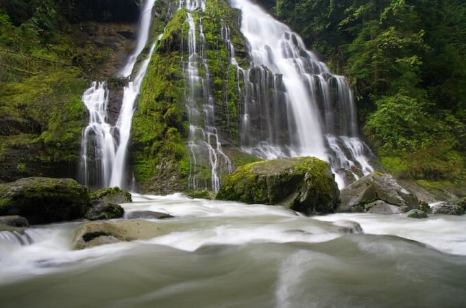 A breathtaking Pacific Northwest waterfall cascading over moss-covered rocks into a tranquil river.