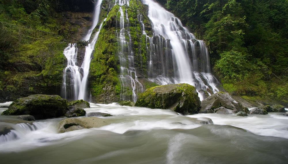 Boulder River A breathtaking Pacific Northwest waterfall cascading over moss-covered rocks into a tranquil river.