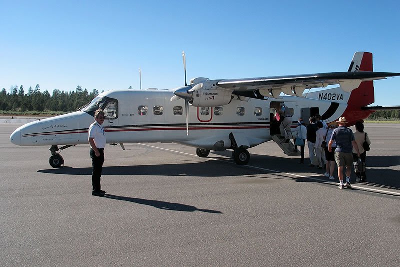 A group of people board a small white and red plane on a sunny airstrip.