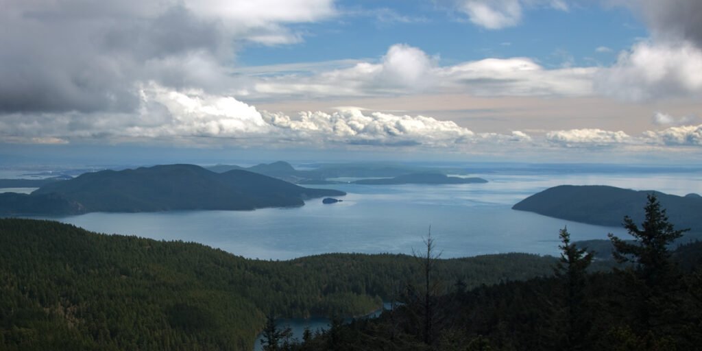 A breathtaking view of rugged coastal islands surrounded by vast blue waters, with lush green forests below under a partly cloudy sky.