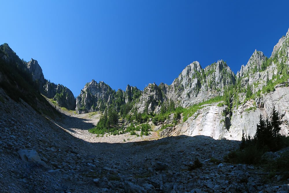 A rocky mountain trail winding through a lush forest under a clear blue sky.
