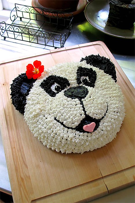 A cute panda-shaped cake made with black and white rice cereal, decorated with a red flower on its ear and a pink heart tongue.