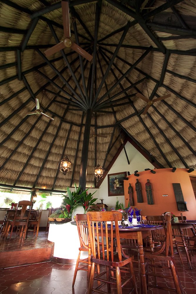 A cozy restaurant interior with a thatched roof and wooden seating, where John and Kristie enjoy a meal together.