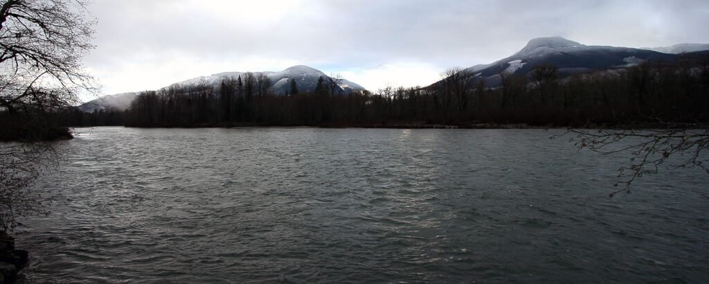 A serene lake surrounded by mountainous terrain and leafless trees under an overcast sky.