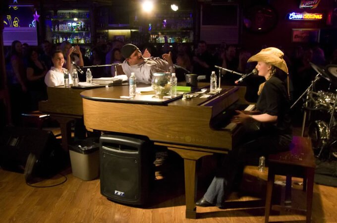 A musician plays piano under warm stage lighting in a dimly lit venue.