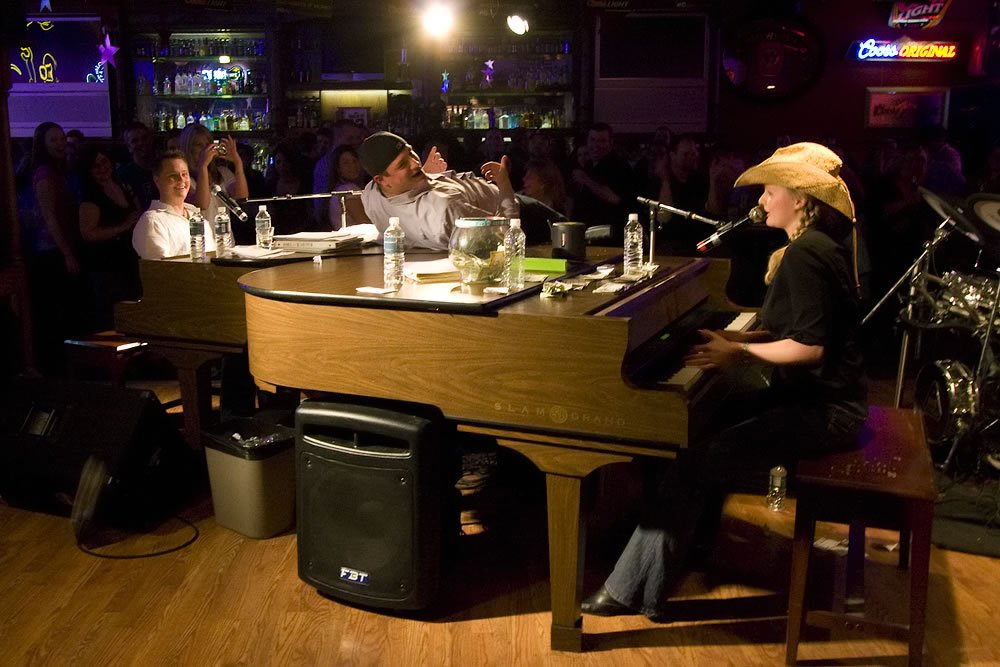 A musician plays piano under warm stage lighting in a dimly lit venue.