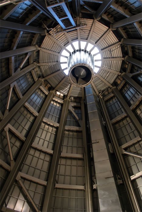 A low-angle view looking straight up into the clock tower room at Pike Place Market. The photo shows the wooden framework, windows, and the mechanism for the iconic face.